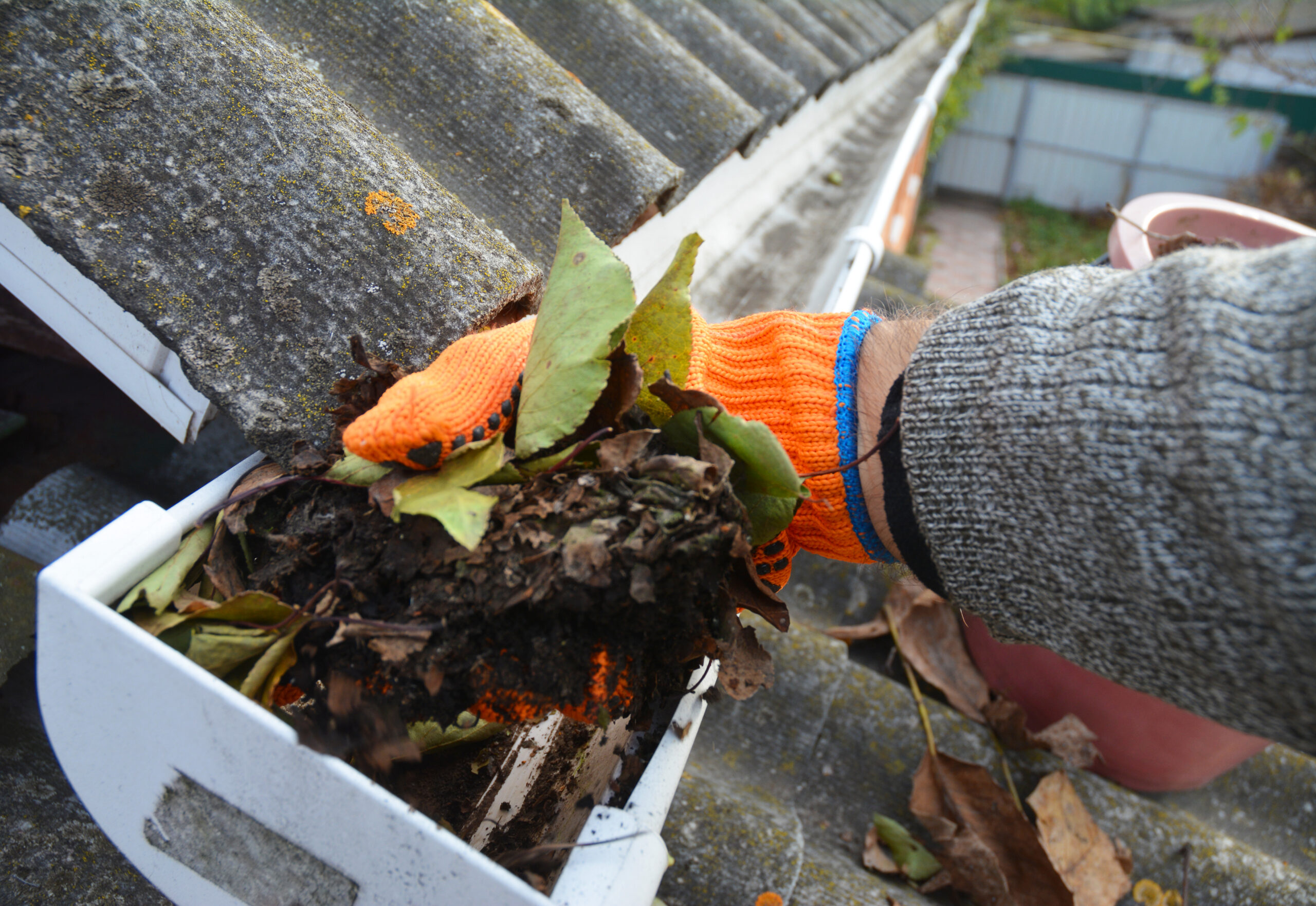 orange gloved hand cleaning a dirty gutter